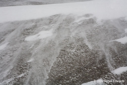 At blizzard's peak, streamers of small snow crystals roar across wind-exposed roadway